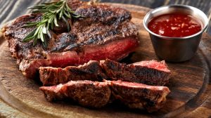 Sliced cooked steak with sauce and rosemary on a wooden plate