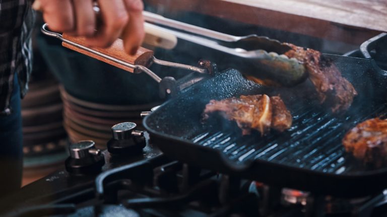 Tongs removing meat from grill pan